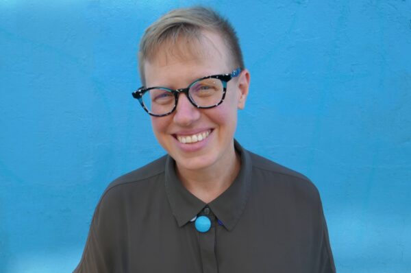 headshot of emily drabinski ala president - smiling, glasses, light blue background