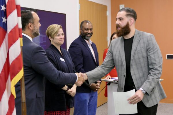 photograph of a man with a beard holding a document shaking another person's hand