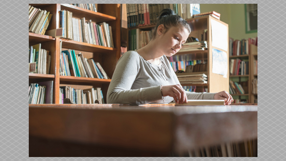 person reading in library at desk in front of book shelves